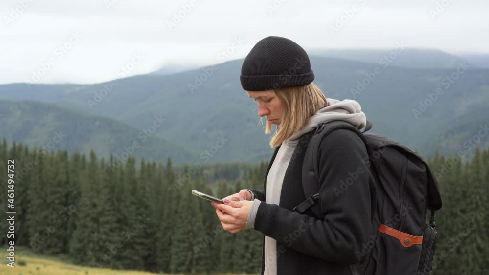 on the top of the mountain a young blonde woman in a hat and with a backpack takes out her cell phone, dials the number and makes a call. Mobile network coverage concept anywhere in the world. on the top of the mountain a young blonde woman in a hat and with a backpack takes out her cell phone, dials the number and makes a call. Mobile network coverage concept anywhere in the world.