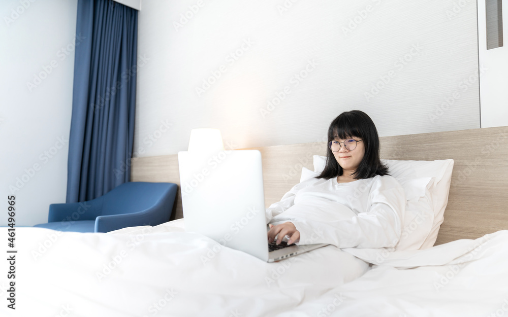Glasses Asian cute woman works and plays laptop notebook on the bed in Work From Home period. Glasses Asian cute woman works and plays laptop notebook on the bed in Work From Home period.
