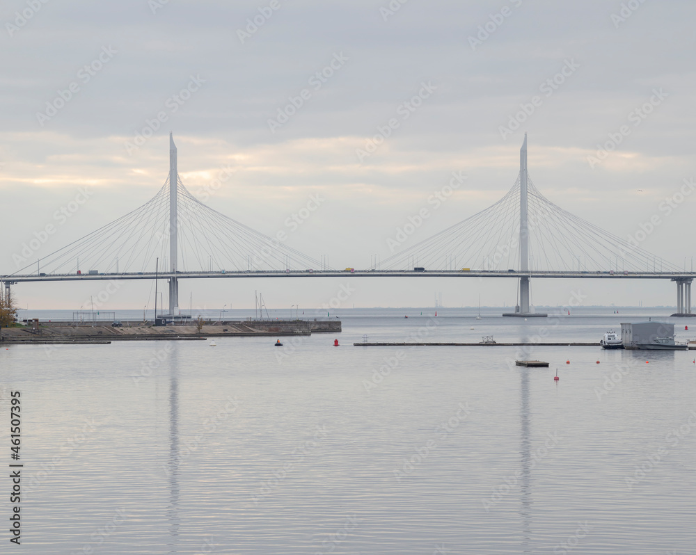 Large elegant cable-stayed bridge with different cars. Reflection of the cable-stayed bridge in calm water.