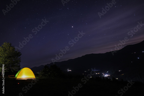 Beautiful view of mountain landscape with glowing yellow camping tent at night