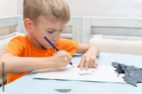 A boy draws and cuts a Halloween decoration at home from black paper. DIY craft decorations. Child makes black bats