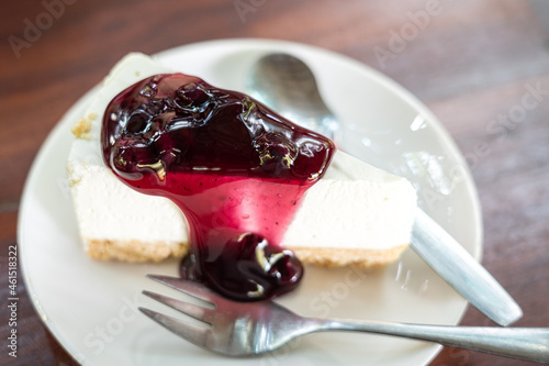 A piece of blueberry cheesecase which is served on table in white plate. Food close-up photo, partial selective focus on the sauce surface.