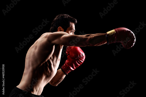 Strong young man punching with boxing gloves on a black background © Ljupco Smokovski