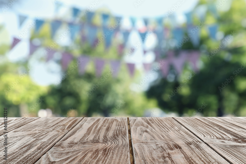 Fototapeta premium Empty wooden table in park decorated with bunting flags, space for design. Outdoor party