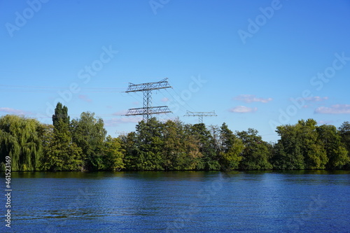 Sonnige Spreelandschaft in Berlin mit grünen Bäumen am Ufer und Strommasten bei blauem Himmel