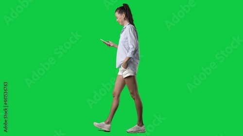 Happy young smart casual summer style woman walking and using cell phone. Side view. Full body on green screen chroma key background