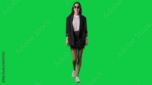 Happy springtime style woman with sunglasses in blazer walking. Full body on green screen chroma key background
