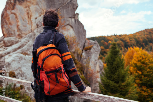 Man traveler with backpack stands by rocks in Tustan in autumn Carpathian mountains. Tourism in Ukraine