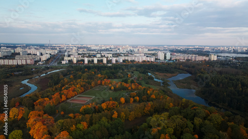 Flight over the autumn park. Trees with yellow autumn leaves are visible. On the horizon there is a blue sky with clouds and city houses. Aerial photography.