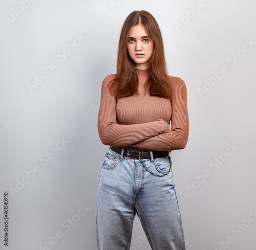 Pretty unhappy angry woman with brunette hair in casual dress looking with folded arms.. Studio shot of good looking beautiful woman against grey studio wall