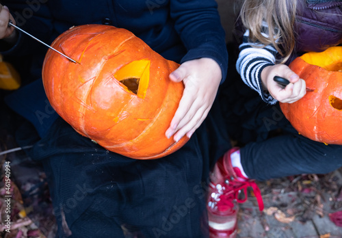 Little girls make jack-o-lantern from big pumpkins for celebratiion of halloween holiday.Witch costume, hat, coat. Cut with knife,take out pulp with seeds.Outdoors activity, backyard.Children's party photo