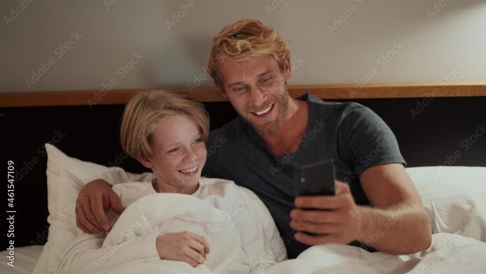 Happy father showing something on the phone to his son in bed Happy father showing something on the phone to his son in bed