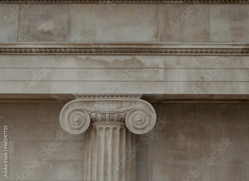 Top part of Ionic style Greek column attached to the marble wall 