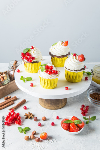 Delicious cupcakes with berries and white cream on a cake pan on a light background. Beautiful cakes with a place for text and for your design