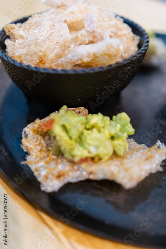 Pork rind with guacamole and bowl of pork rinds on traditional Mexican comal