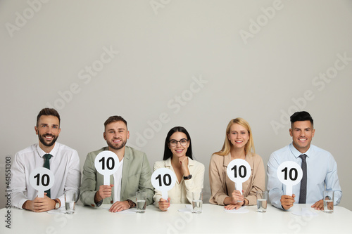 Panel of judges holding signs with highest score at table on beige background