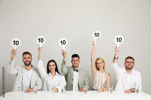 Panel of judges holding signs with highest score at table on beige background photo