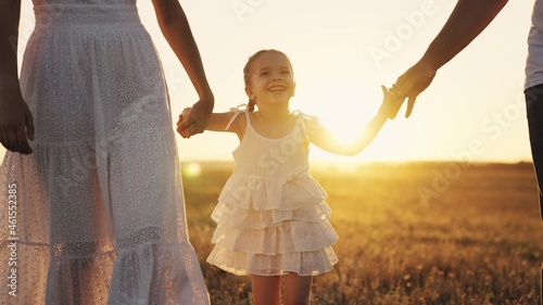 girl leads her mother and father by the hand at sunset, a little daughter with her parents in the sunshine, hold hand in hand, a happy family, a child with mom and dad, take care of and love the baby