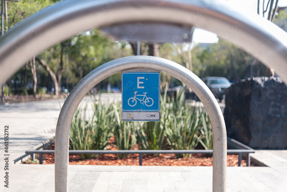 Blue bicycle parking spot sign on metal arch with trees as background