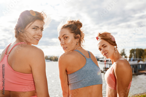 Happy women in fitness clothes relaxing and having fun in the park by the river. Fitness  sport  friendship and healthy lifestyle concept . Group of happy people exercising