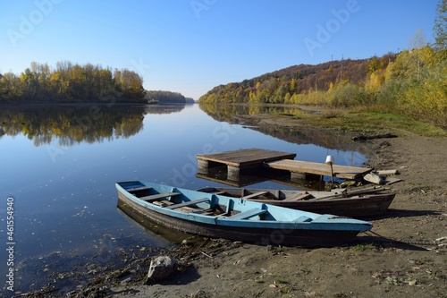 On the river bank near the pier there are two wooden boats against the background of the autumn forest 