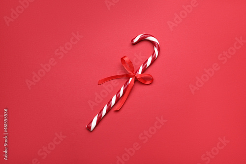 Sweet Christmas candy cane with bow on red background, top view