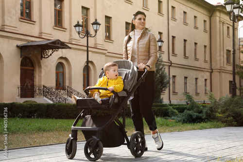Happy mother walking with her son in stroller outdoors photo