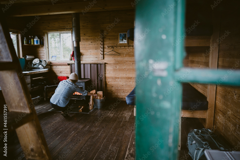 View through doorway of a woman stoking fire inside rustic cabin View through doorway of a woman stoking fire inside rustic cabin