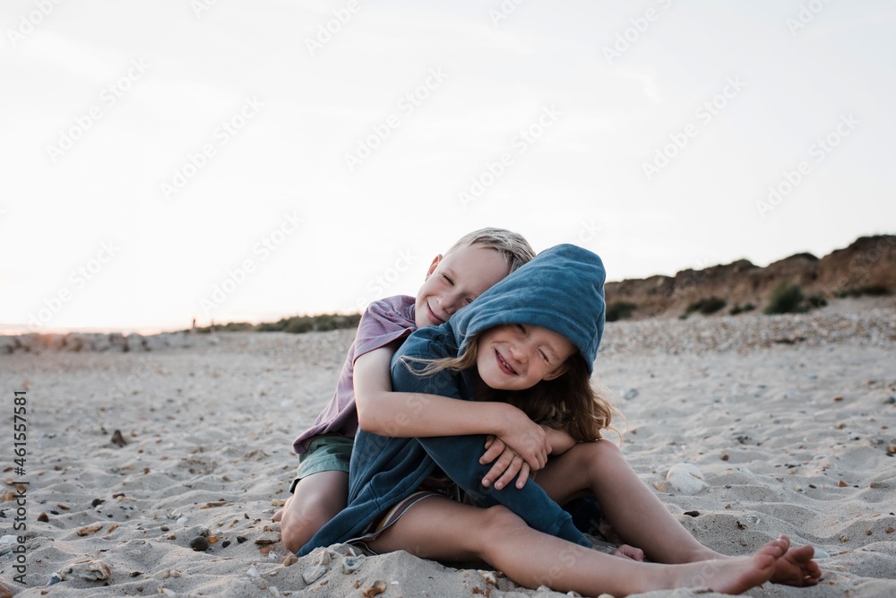 brother and sister sat on sand playfully hugging at the beach brother and sister sat on sand playfully hugging at the beach