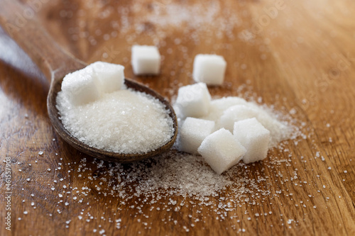 Sugar in wooden spoon, on wooden table