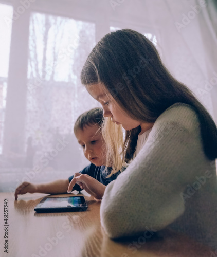Little girl and boy playing on a gadget tablet pc at home at the table photo