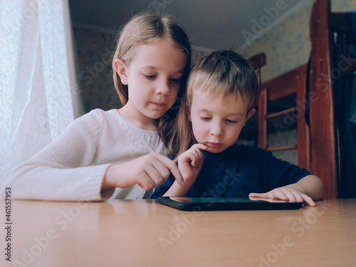 Two little kids with gadget tablet at home at the table photo