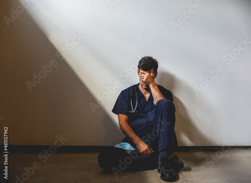 Exhausted doctor wearing scrubs sitting on floor in a patch of light. photo