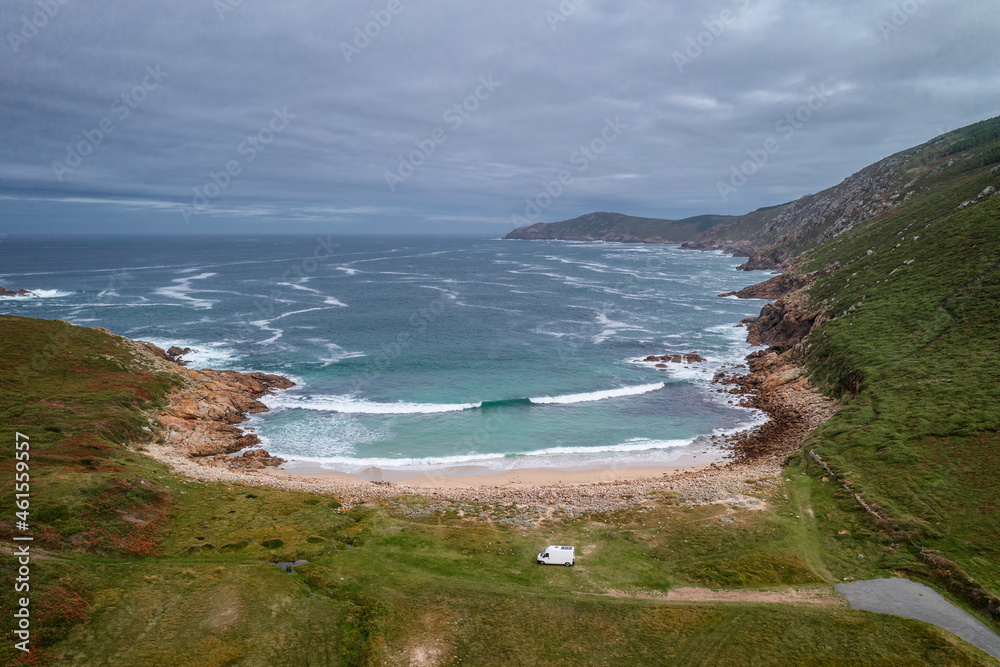 Drone aerial view of a camper van on a wild beach with green landscape in Galicia, Spain