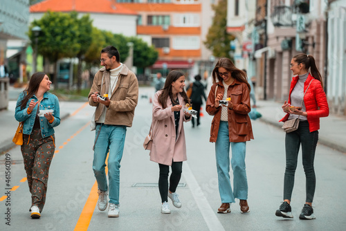 A group of young people dressed in modern clothes talk while walking around the city and eating sweets. Selective focus