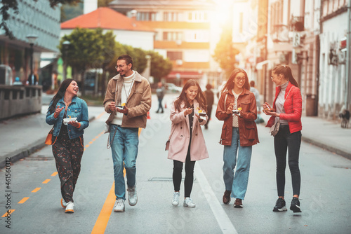 A group of young people dressed in modern clothes talk while walking around the city and eating sweets. Selective focus