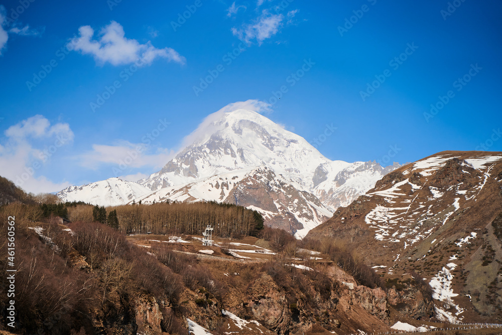 Automobile mountain road to the bottom of Mount Kazbegi. Snow cap on the top of the mountain
