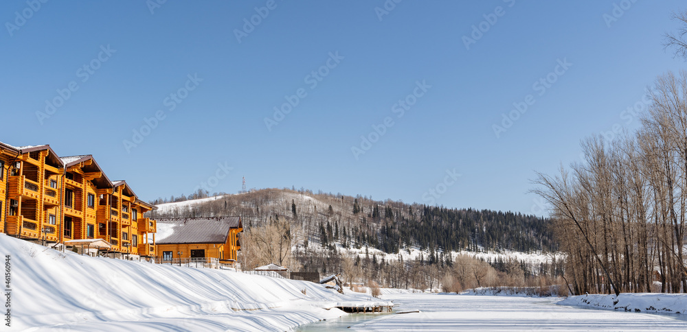 Panoramic view of the frozen and snow-covered lake and large country houses on the shore. Ahead of the mountains and pine forests. Active rest in winter, fascinating nature