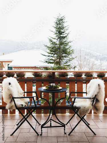 Winter balcony with coffee table, cozy chairs covered with white fur and splendid snow-covered mountains view. Winter vacation