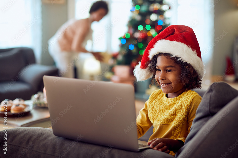 Happy black little girl surfing the net on laptop on Christmas day at home. Happy black little girl surfing the net on laptop on Christmas day at home.
