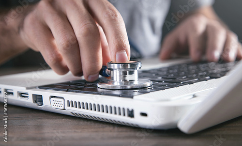 Male hand holding stethoscope on a laptop keyboard.