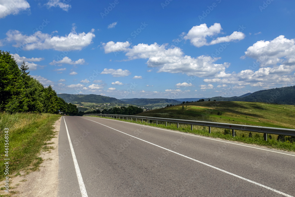 Asphalt road in a mountain in the woods, on the background of a blue sky with white clouds, Ukraine, Carpathians