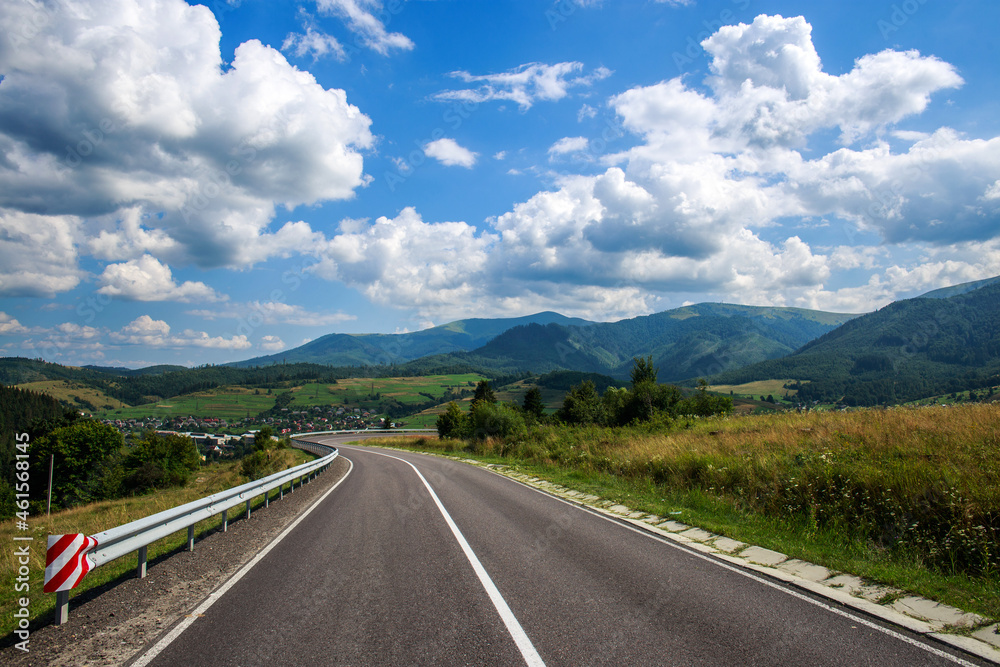 Asphalt road in a mountain in the woods, on the background of a blue sky with white clouds, Ukraine, Carpathians Asphalt road in a mountain in the woods, on the background of a blue sky with white clouds, Ukraine, Carpathians
