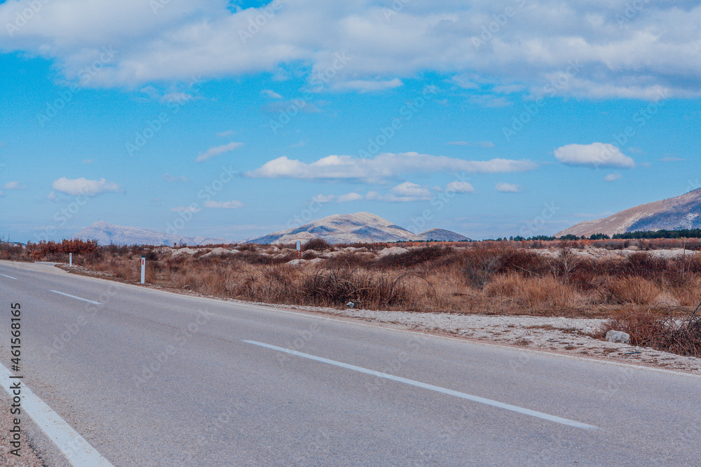 The Asphalt road in the mountains. Landscape view perspective of mountain road with white clouds on blue sky. Traveling by car. Design element of road The Asphalt road in the mountains. Landscape view perspective of mountain road with white clouds on blue sky. Traveling by car. Design element of road
