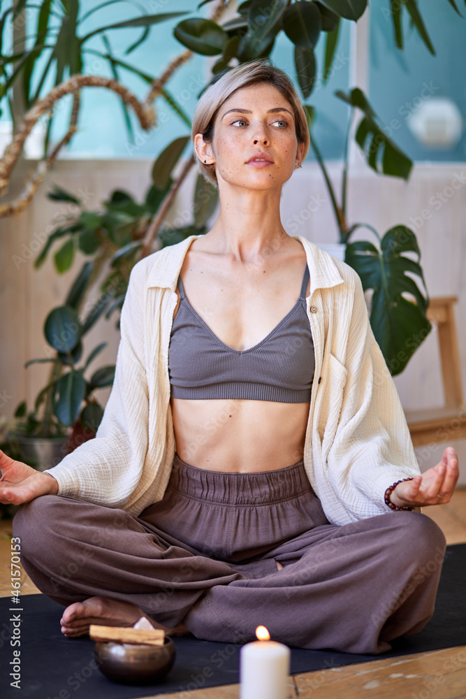 Confident female doing yoga exercise at home, sitting on floor. Mindfulness meditation. Relax breathe easy pose, healthy lifestyle concept. Burning candles light. Atmosphere of relax and zen.