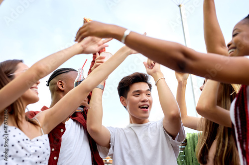 group of excited friends, young diverse men and women doing barbecue in nature, raising hands with beverages, celebrating the end of exams, have fun at picnic, summer time concept, friendship