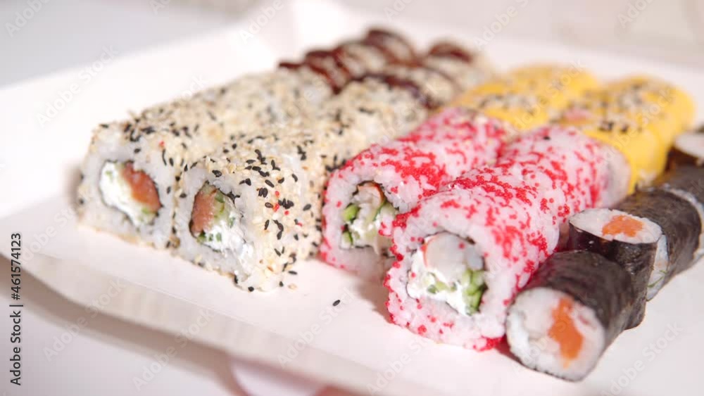 A person with the help of a hand and disposable chopsticks takes sushi philadelphia in tobiko caviar with shrimp from the set from the delivery. Paper eco-friendly packaging with a set of rolls on a A person with the help of a hand and disposable chopsticks takes sushi philadelphia in tobiko caviar with shrimp from the set from the delivery. Paper eco-friendly packaging with a set of rolls on a
