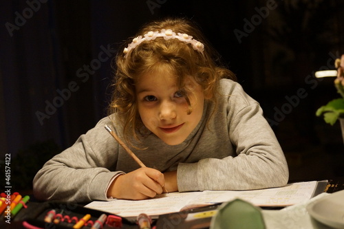 Junges Mädchen sitzt an einem Tisch und macht Hausaufgaben. Sie lernt fleißig. Es ist spät, der Hintergrund ist dunkel. 