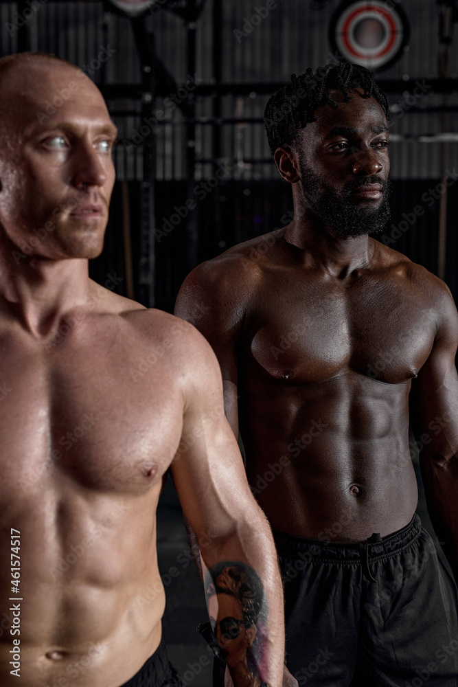 Workout. Crossfit. Extreme. Training. Portrait of two interracial shirtless sportsmen before or after cross fit training, strong men with perfect body, abs muscles. focus on black man in background