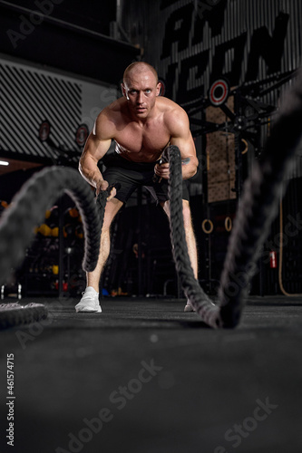Waves of force. Young caucasian healthy bodybuilder training with battle ropes. Fit strong single male model training with battle rope. Concept of sport, bodybuilding, healthy lifestyle.